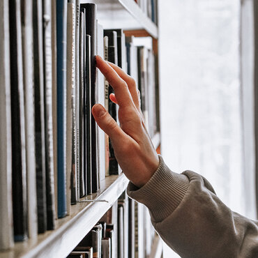 Eine Hand streicht durch Bücher in einem Regal.