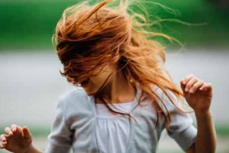 Mädchen mit roten Haaren tanzt mit gehobenen Armen. 