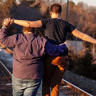 Zwei Personen gehen Hand in Hand an Bahngleisen entlang.