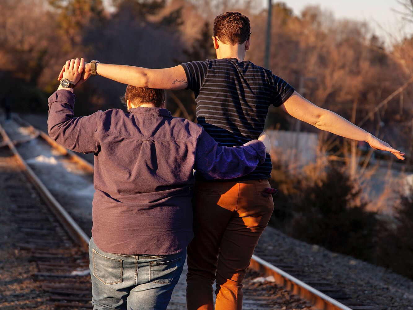 Zwei Personen gehen Hand in Hand an Bahngleisen entlang.
