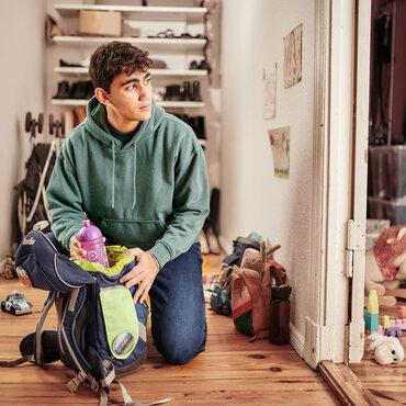 Ein junger Mensch kniet in einem Hausflur und packt einen Rucksack