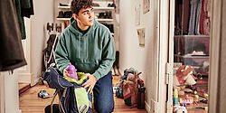 Ein junger Mensch kniet in einem Hausflur und packt einen Rucksack