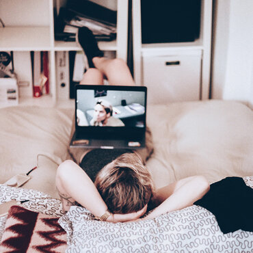 Eine Person liegt auf dem Bett und schaut eine Serie auf dem Laptop.