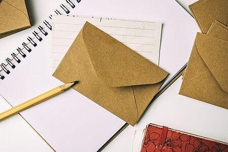 Mehrere Briefumschläge und ein Schreibblock mit einem Bleistift auf weißer Tischoberfläche