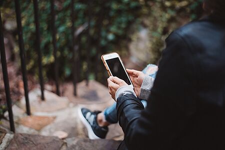 Eine Person sitzt auf einer Treppe und hält ein Handy in der Hand.