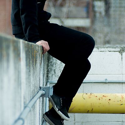 Junge sitzt auf einer Mauer und lässt die Beine baumeln.